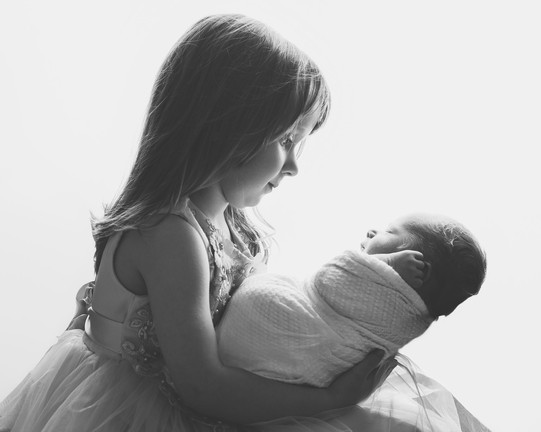 Black and white phtoo of a five year old girl holding her new baby brother in her arms by Newborn photographer in Somerset, Wiltshire and Bath