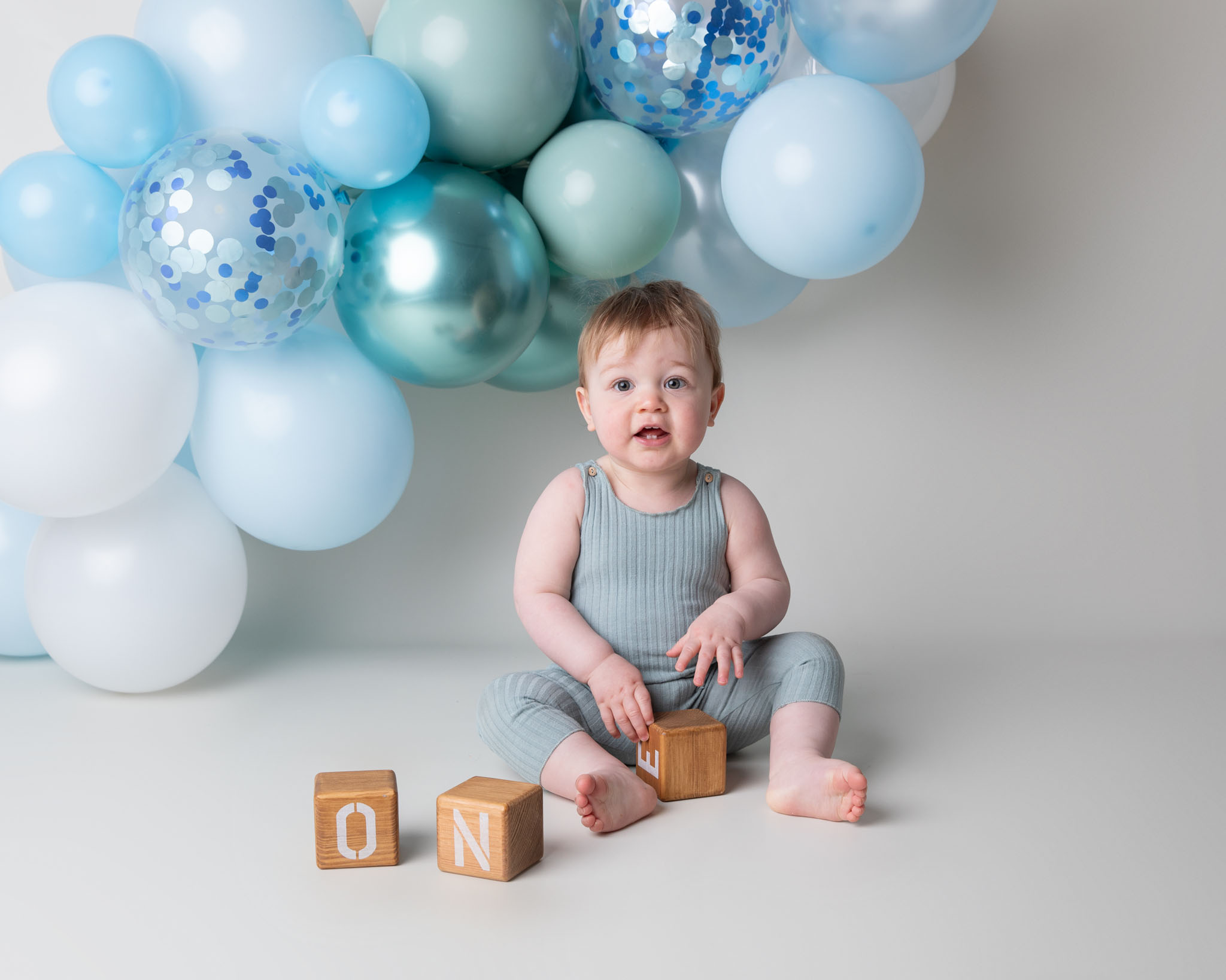 baby boy with blue balloons behind him at a first birthday photoshoot by cake smash photographer in wiltshire and somerset