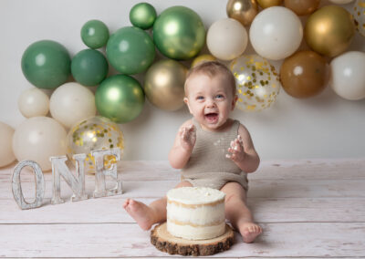 baby boy in a cream romper with balloons and a birthday cake at a cake smash photoshoot by Family and portrait photography in Wiltshire, Somerset and Bath